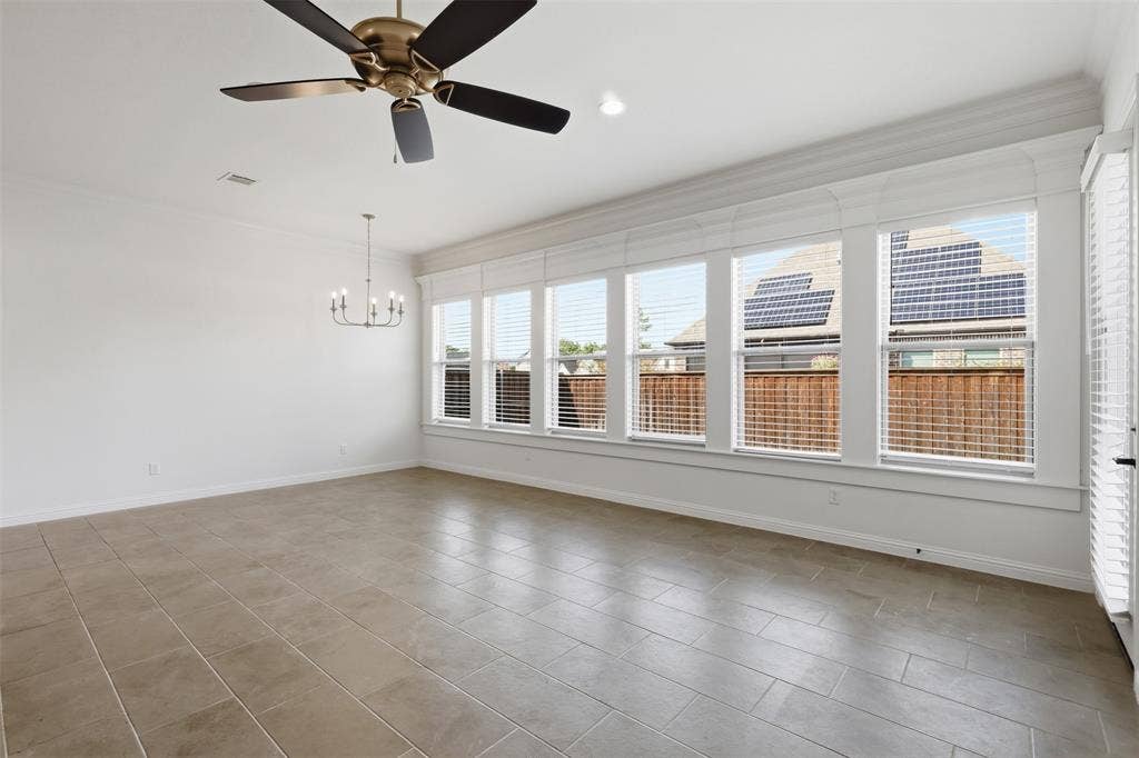 Large interior space featuring neutral tile flooring, expansive multi-pane windows with trim detailing, a tiered chandelier, and a ceiling fan with integrated lighting