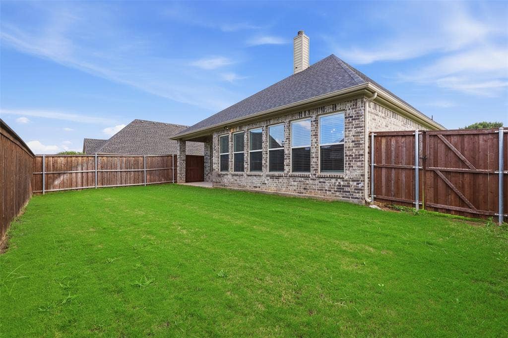 Backyard featuring a manicured lawn, brick exterior, shingled hip roof, chimney, and wooden privacy fencing
