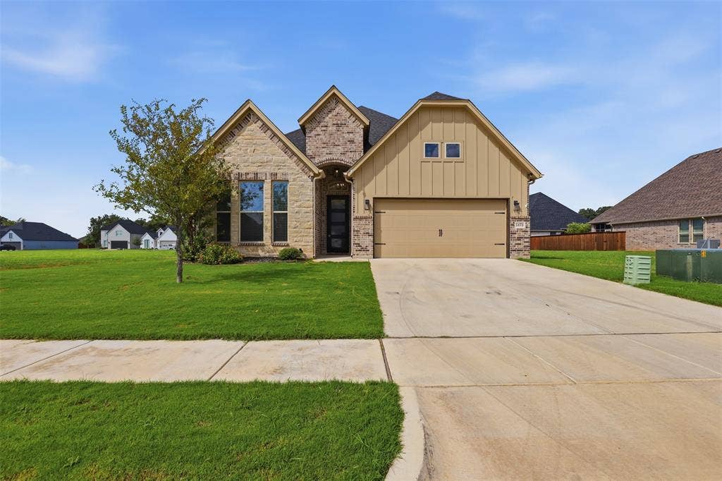 Exterior facade featuring a combination of stone and vertical siding, a front-facing attached two-car garage, and a concrete driveway