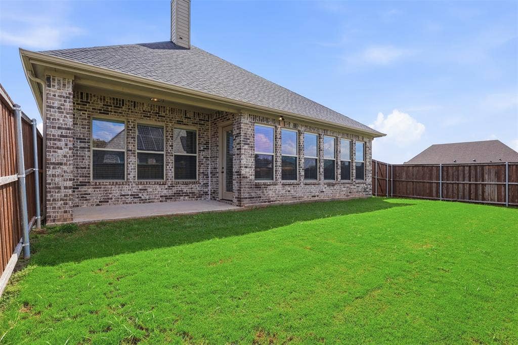 Brick exterior with covered patio, gabled roofline, and wood-panel perimeter fencing surrounding a level lawn