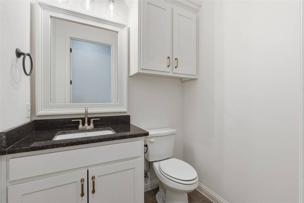 White shaker-style cabinetry with metallic hardware, dark stone countertop, undermount sink, matching wall-mounted cabinet, and framed mirror
