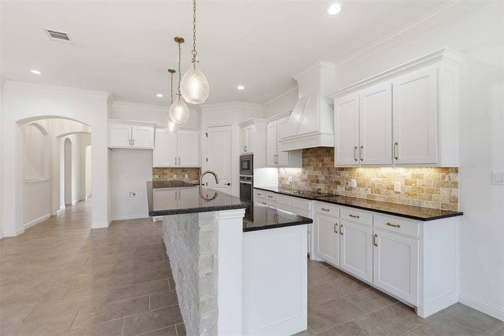 Kitchen featuring white shaker cabinetry, dark stone countertops, stone backsplash, built-in stainless steel appliances, and a central island with stone detailing