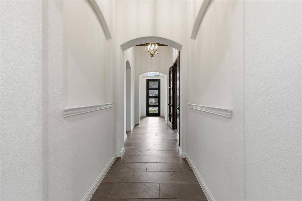 Arched passageways with recessed wall niches, crown molding, tile flooring, and multi-light pendant fixture