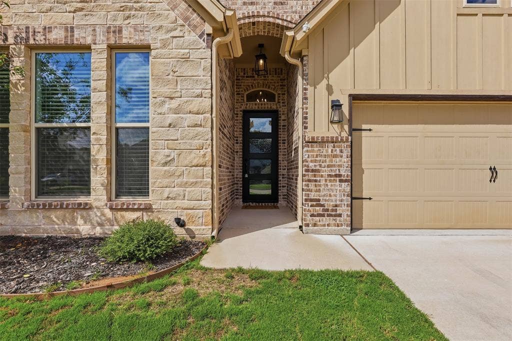 Exterior featuring a stacked-stone facade, vertical board-and-batten siding, arched entryway with a multi-pane glass door, and a concrete driveway