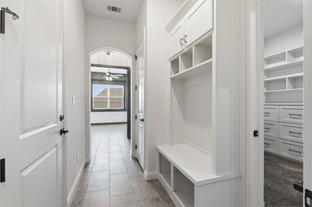 Built-in mudroom cabinetry with beadboard detailing, ceramic tile flooring, arched architectural passage, and custom closet storage with integrated shelving and drawers
