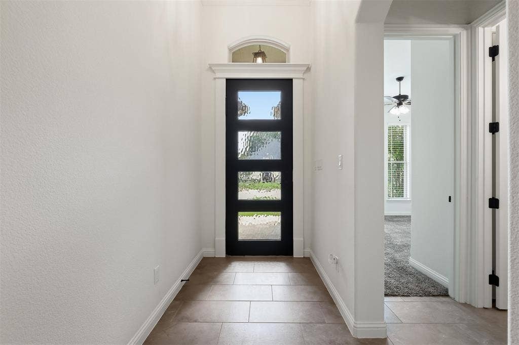 Foyer featuring large-format tile flooring, a modern black four-panel door with textured glass inserts, and a decorative arched transom window