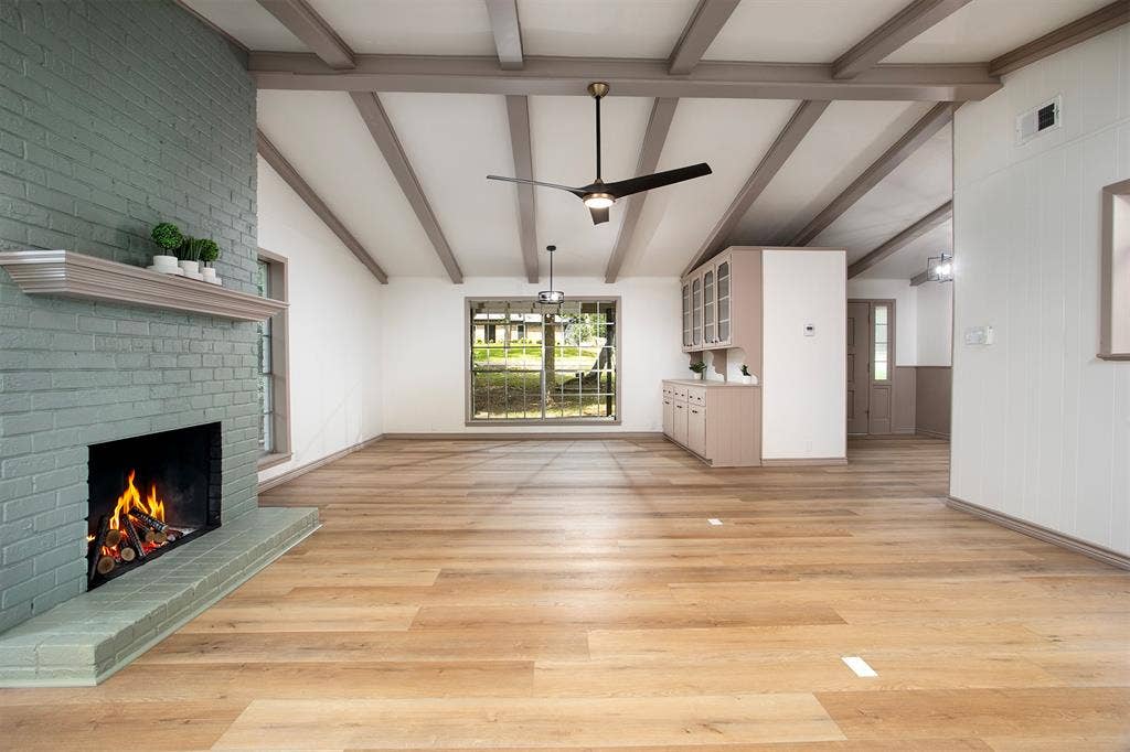 431 Lone Star Lane, Hideaway, TX 75771 Painted brick fireplace with a wood mantel, exposed ceiling beams, wood-finish flooring, and built-in cabinetry with glass-front uppers