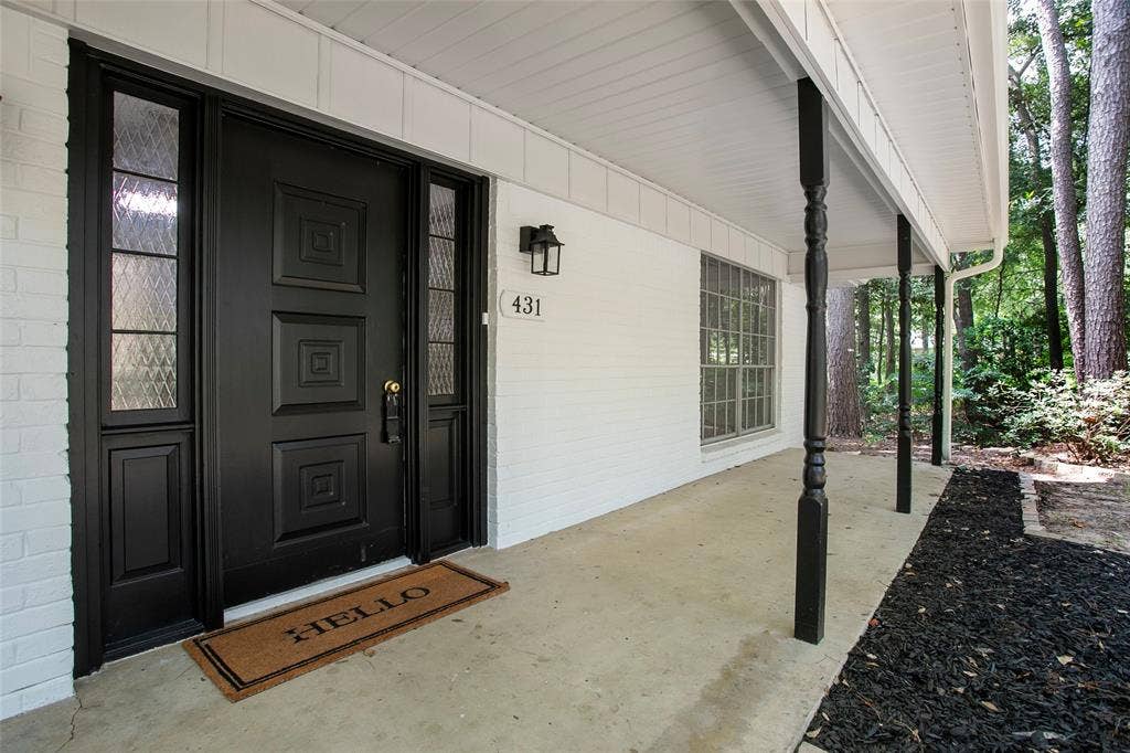 431 Lone Star Lane, Hideaway, TX 75771 Covered front porch featuring a white painted brick facade, black paneled door with glass sidelights, and decorative turned support columns