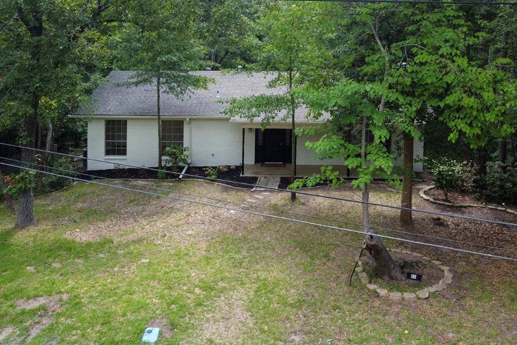 431 Lone Star Lane, Hideaway, TX 75771 White-painted brick exterior featuring a covered front porch, asphalt shingle roof, and established mature trees