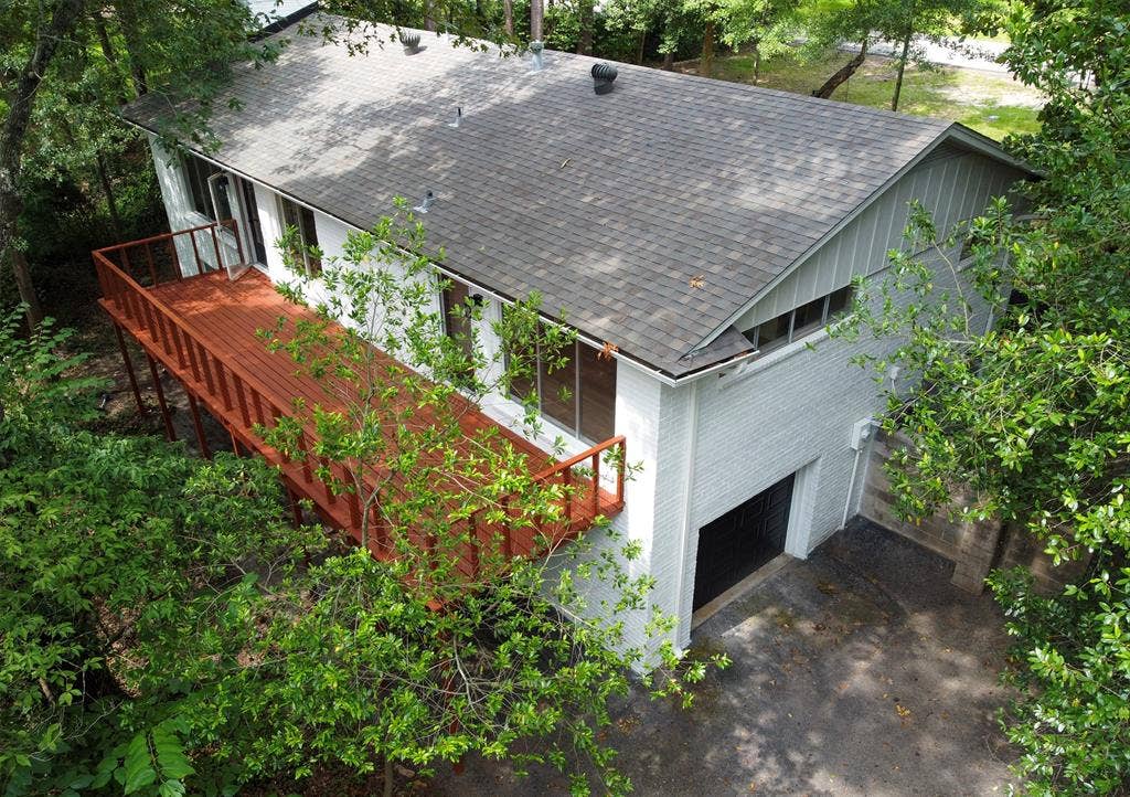 431 Lone Star Lane, Hideaway, TX 75771 White brick exterior featuring an expansive wood deck, asphalt shingle roof, vertical siding accents, and a ground-level garage
