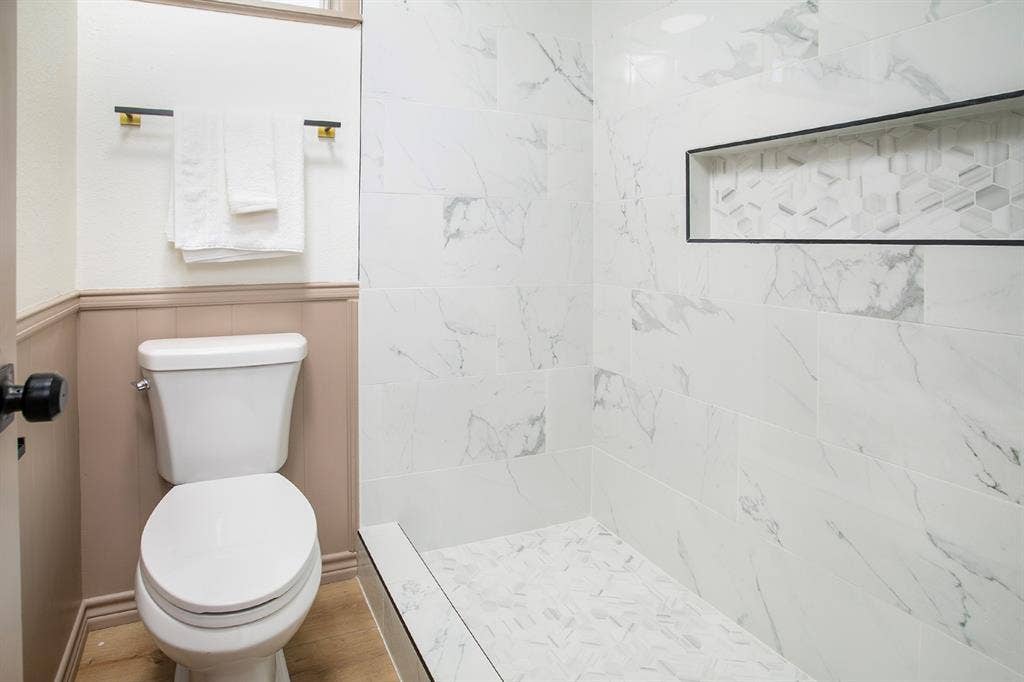 431 Lone Star Lane, Hideaway, TX 75771 Walk-in shower featuring large-format stone-finish wall tile, a geometric-patterned inset storage niche, a mosaic-tiled floor, and wood-finish flooring