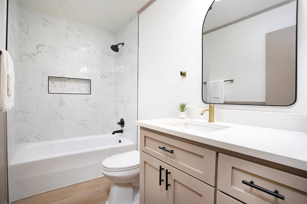 431 Lone Star Lane, Hideaway, TX 75771 Bathroom featuring a vanity with white countertop, arched wall-mounted mirror, wood-finish flooring, and a tub-shower combination with built-in niche and contrasting fixtures