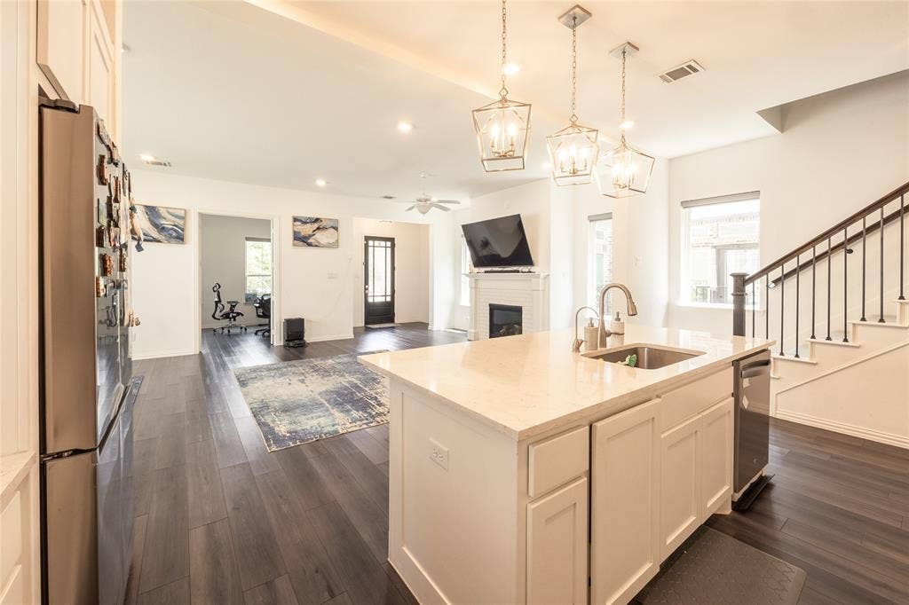 Kitchen featuring a center island with a stone-finish countertop and undermount sink, pendant lighting, wood-finish flooring, and a fireplace with a decorative mantel