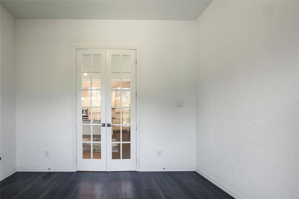 White French doors featuring glass panes and dark-toned hardware, set against dark wood-finish flooring
