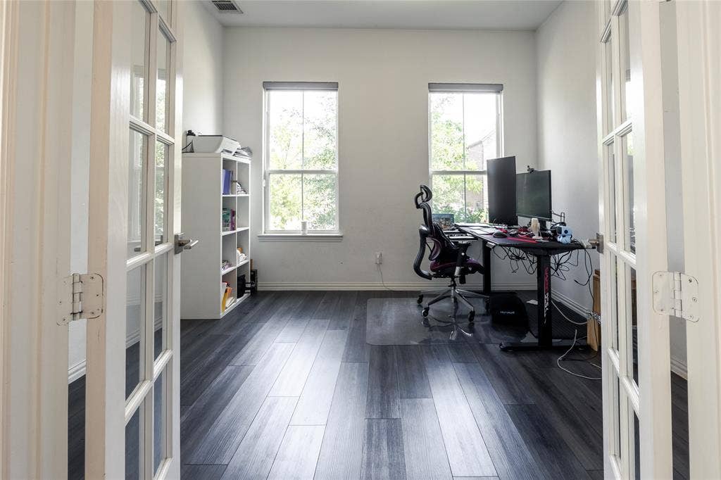 Room featuring dual French doors, wood-finish flooring, and two oversized windows with neutral roller shades