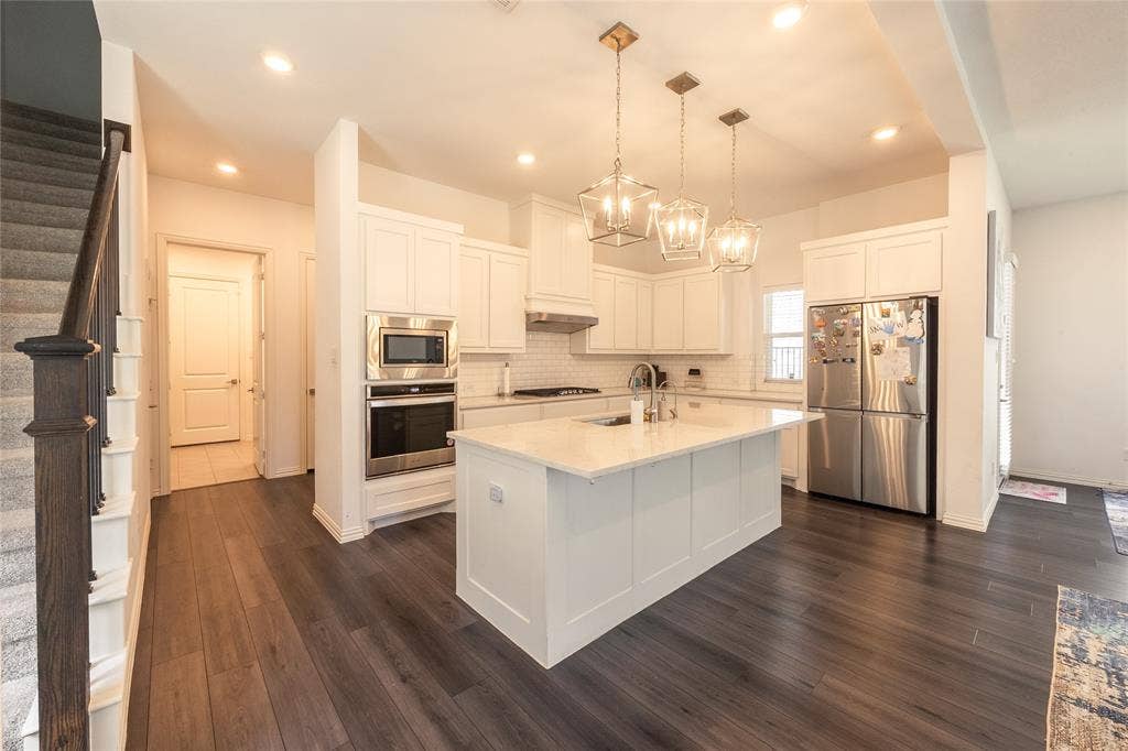 Kitchen featuring a central island with a stone countertop, white cabinetry, built-in double wall ovens, recessed lighting, and wood-finish flooring