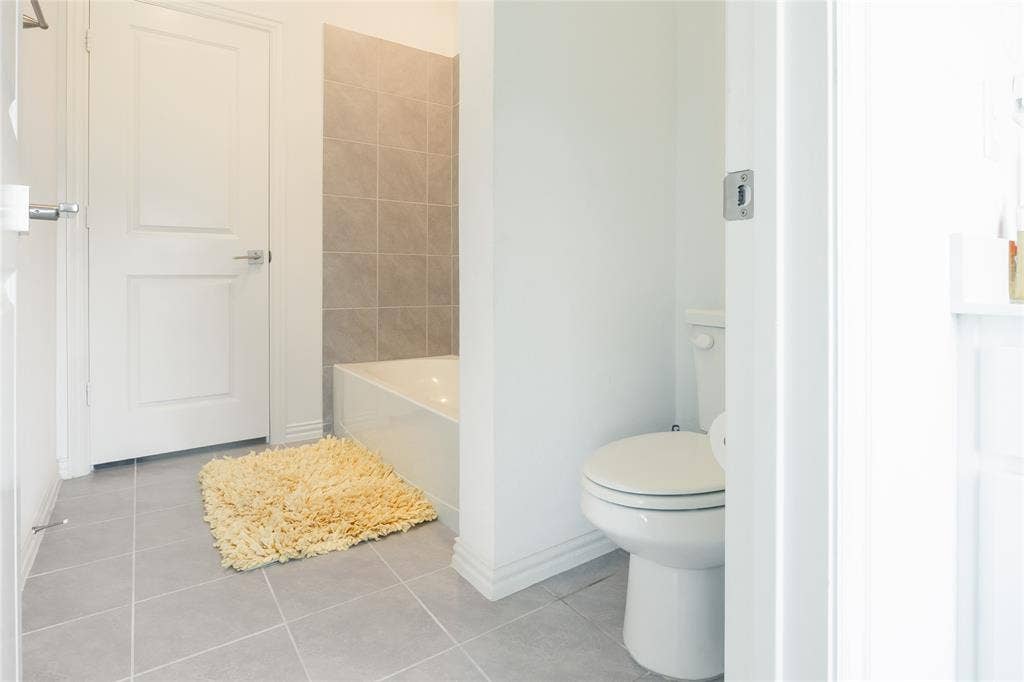 Bathroom featuring grey tile flooring, a bathtub with neutral wall tile surround, and a white toilet