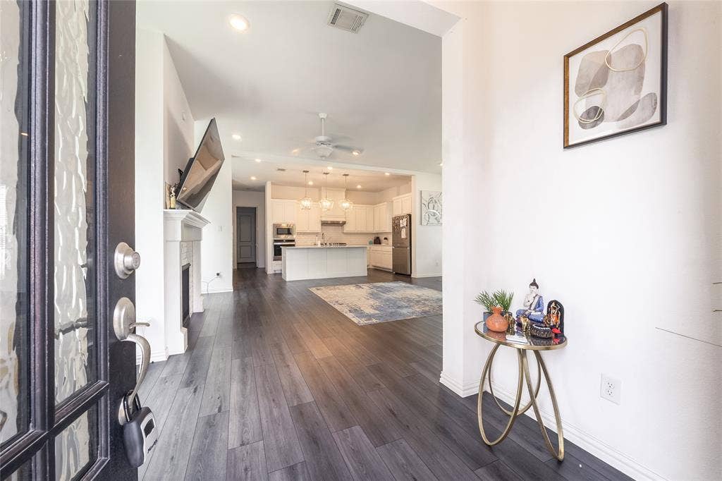 Entryway featuring a dark-framed glass-panel door, wood-finish flooring, and a fireplace with a decorative mantel, extending toward a kitchen with white cabinetry and a center island