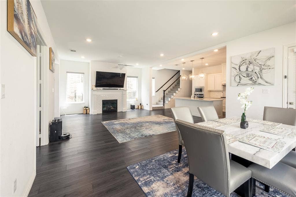 Open-concept interior featuring wood-finish flooring, a white brick-surround fireplace, recessed lighting, and a kitchen island with pendant fixtures