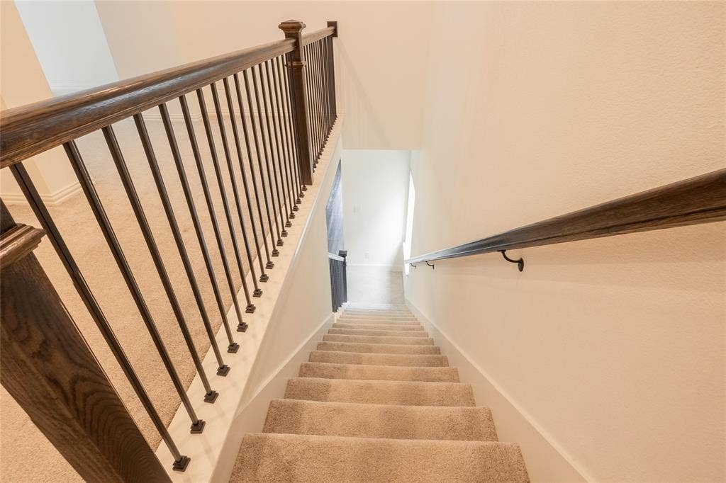 Staircase featuring a dark wood handrail, metal vertical balusters, square newel posts, and neutral carpeting