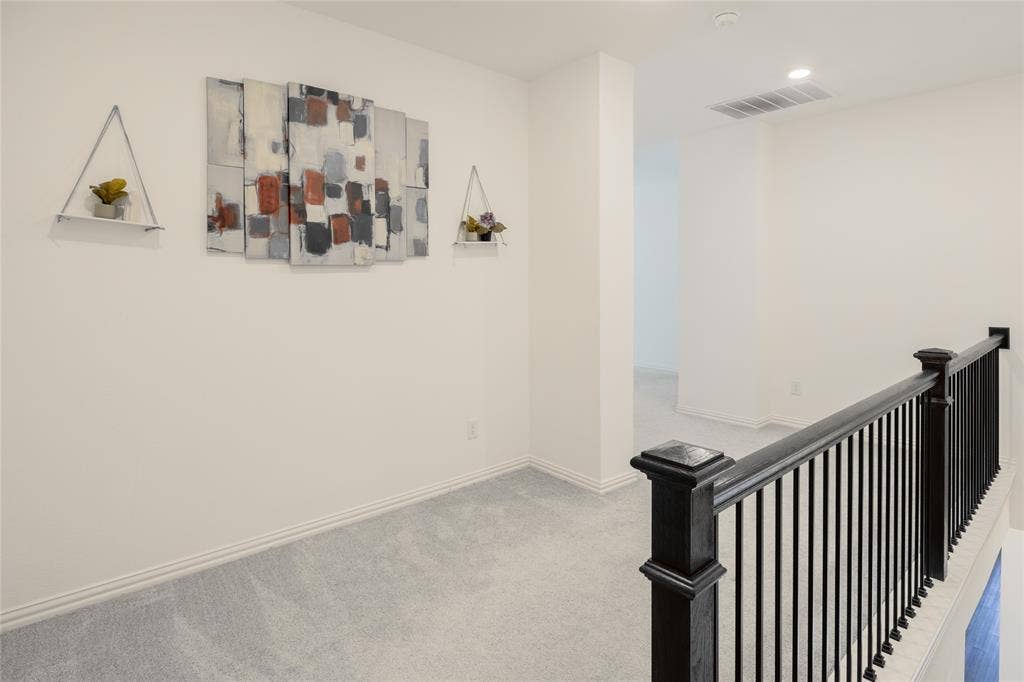 Neutral-toned carpeted hallway featuring recessed ceiling lighting, a dark wood railing with black metal spindles, and white walls