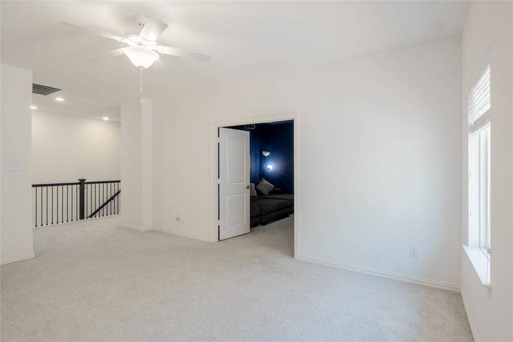 Room featuring neutral wall-to-wall carpeting, ceiling fan with integrated lighting, dual-panel interior door, and a metal baluster staircase railing