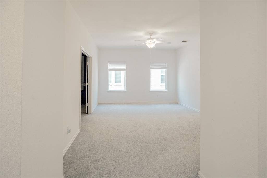 Interior space featuring neutral wall-to-wall carpeting, dual windows with roller shades, and a ceiling-mounted light fixture with fan blades