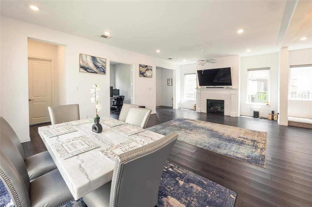 Open-concept living space featuring wood-finish flooring, recessed lighting, and a white brick fireplace with a decorative mantel