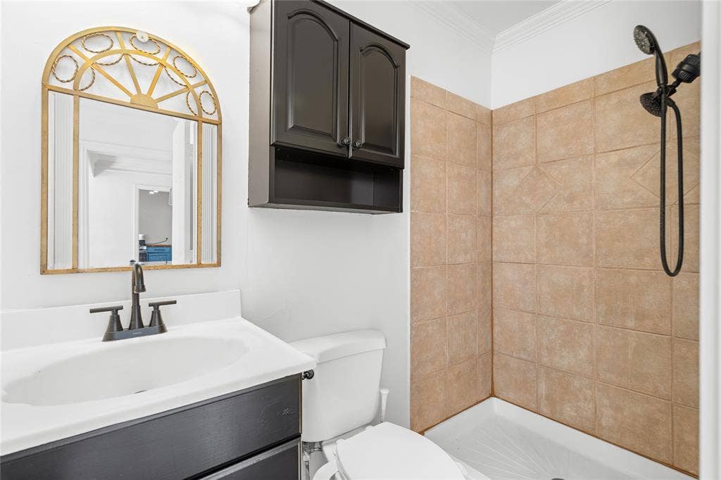 2005 Tisinger Avenue, Dallas, TX 75228 Bathroom featuring a vanity with dark cabinetry, integrated countertop, and matte black faucet, wall-mounted dark storage cabinet, and tiled shower enclosure with a handheld shower head