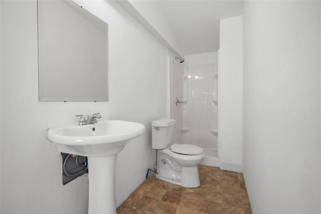 2005 Tisinger Avenue, Dallas, TX 75228 Pedestal sink with chrome faucet, wall-mounted mirror, two-piece toilet, and shower enclosure with integrated shelving