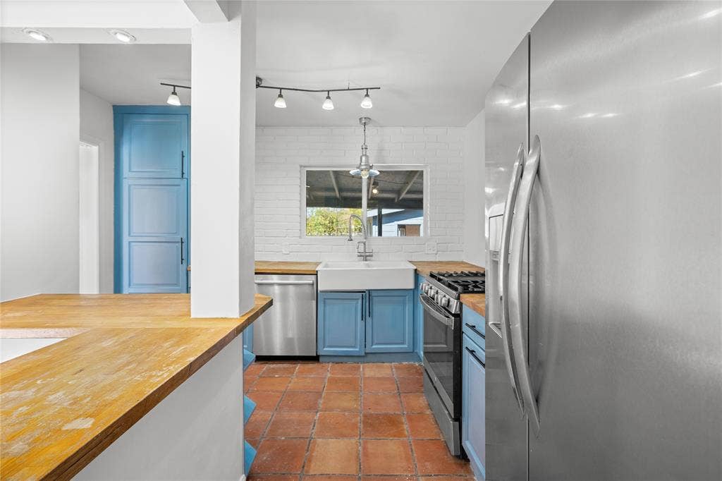 2005 Tisinger Avenue, Dallas, TX 75228 Kitchen featuring a ceramic farmhouse sink, wood-finish countertops, stainless steel appliances, blue cabinetry, and terra-cotta tile flooring