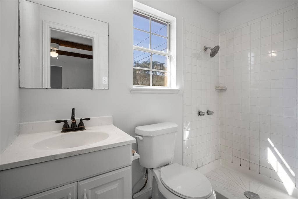2005 Tisinger Avenue, Dallas, TX 75228 Bathroom featuring a vanity with an integrated sink and bronze-finish faucet, a wall-mounted frameless mirror, a single-hung window, and a tiled shower enclosure