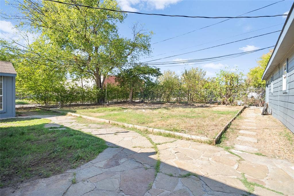 2005 Tisinger Avenue, Dallas, TX 75228 Backyard space featuring stone hardscaping, a raised garden bed with timber edging, chain-link perimeter fencing, and mature trees