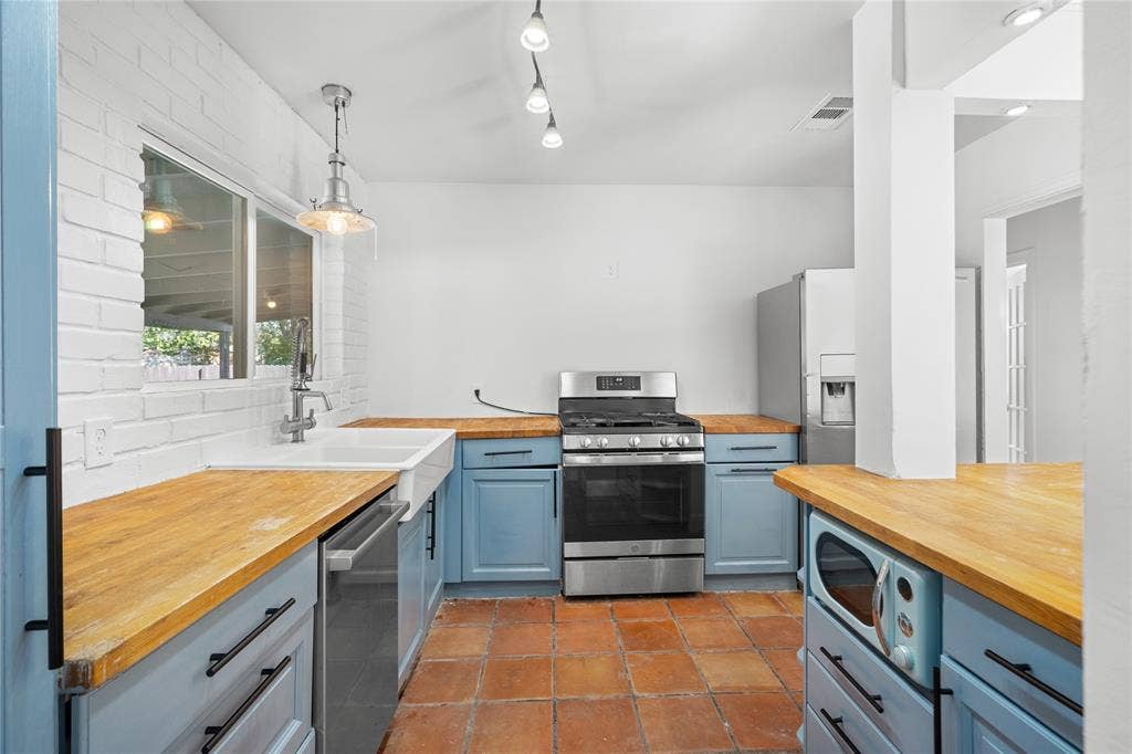 2005 Tisinger Avenue, Dallas, TX 75228 Kitchen featuring blue cabinetry, wood countertops, a white apron-front sink, stainless steel appliances, and terracotta tile flooring