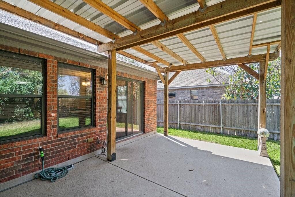 Covered patio featuring a concrete slab, red brick exterior wall, sliding glass door, and timber-frame pergola with a corrugated metal roof