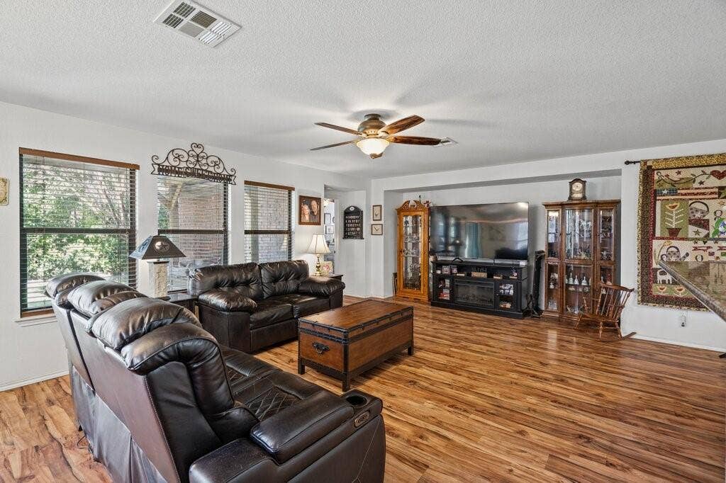 Living area featuring wood-finish flooring, a recessed media alcove, and a multi-blade ceiling fan