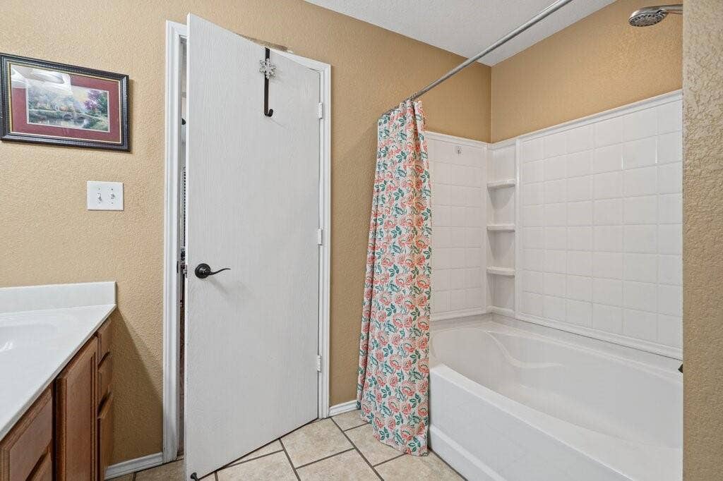 Bathroom featuring a built-in tub and shower combination with tile-surround wall paneling and integrated shelving, stone-finish tile flooring, and a wooden vanity cabinet with a white countertop