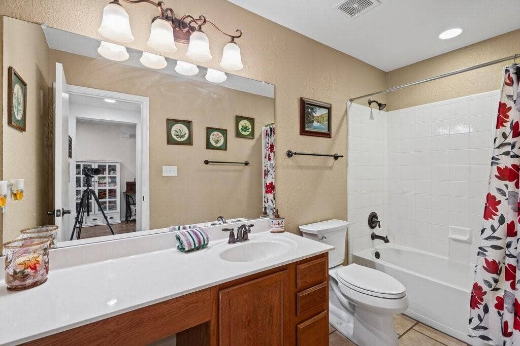 Bathroom featuring wood-finish cabinetry, white solid-surface countertop with an integrated oval sink, full-width wall mirror, multi-light vanity fixture, and a tub-shower combination with white tile surround