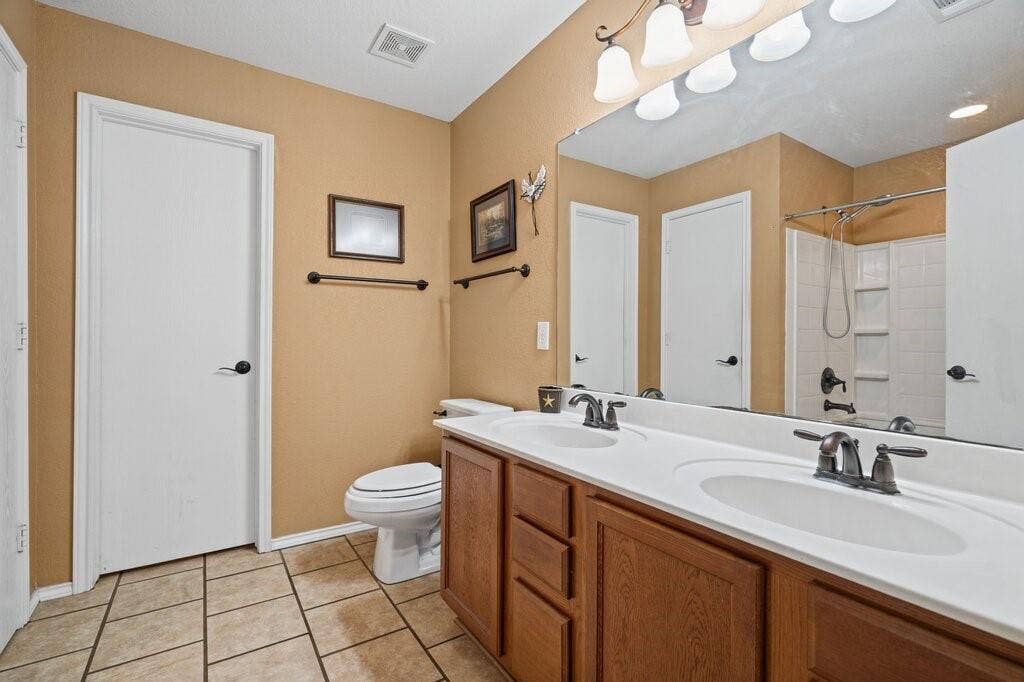 Dual-sink vanity with dark hardware, a large frameless wall mirror, tile flooring, and a combined tub and shower enclosure