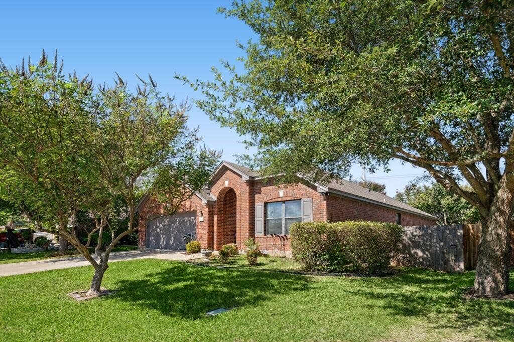 Single-story brick exterior featuring an arched entryway, shingled roof, attached garage, and mature landscaping