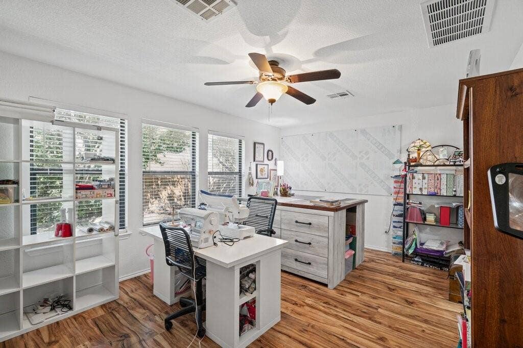 Room featuring wood-finish flooring, three windows with horizontal blinds, and a central ceiling fan with integrated lighting