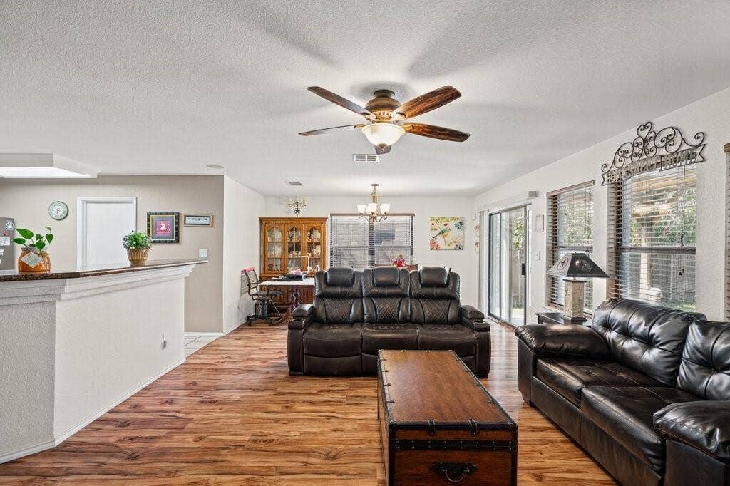 Open-concept interior featuring wood-finish flooring, a central ceiling fan with integrated lighting, a raised kitchen counter, and sliding glass doors