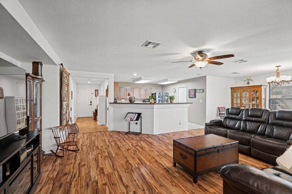 Living area featuring wood-finish flooring, recessed ceiling lighting, a multi-blade ceiling fan with integrated light fixture, and a peninsula counter