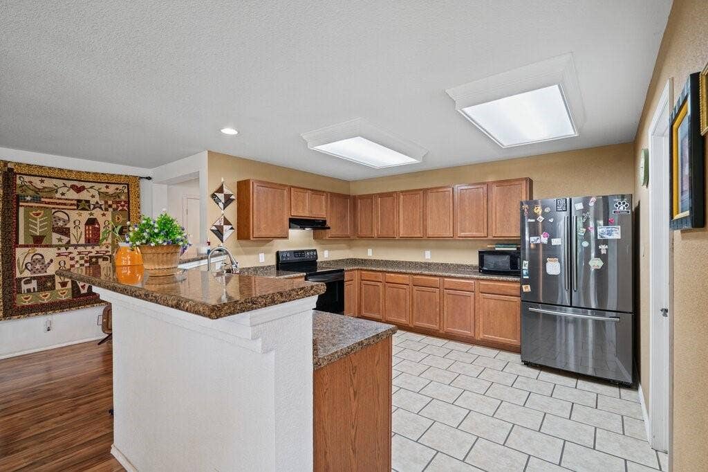 Kitchen featuring wood cabinetry, stone-finish countertops, tile flooring, and integrated stainless steel refrigerator