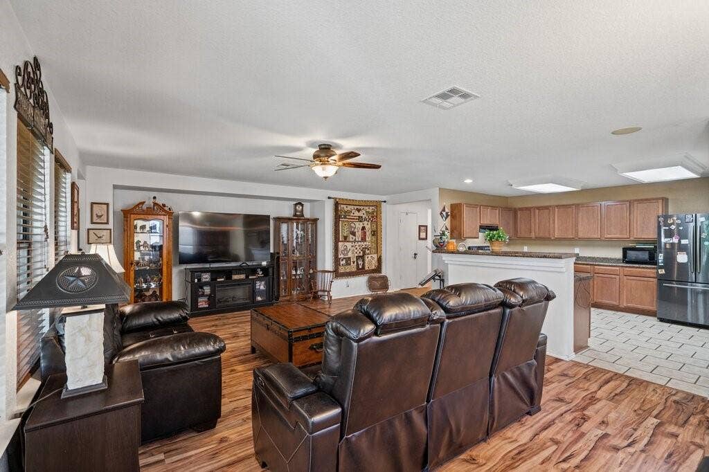 Open-concept interior featuring wood-finish flooring, recessed built-in shelving, a ceiling fan, and kitchen cabinetry with a raised breakfast bar