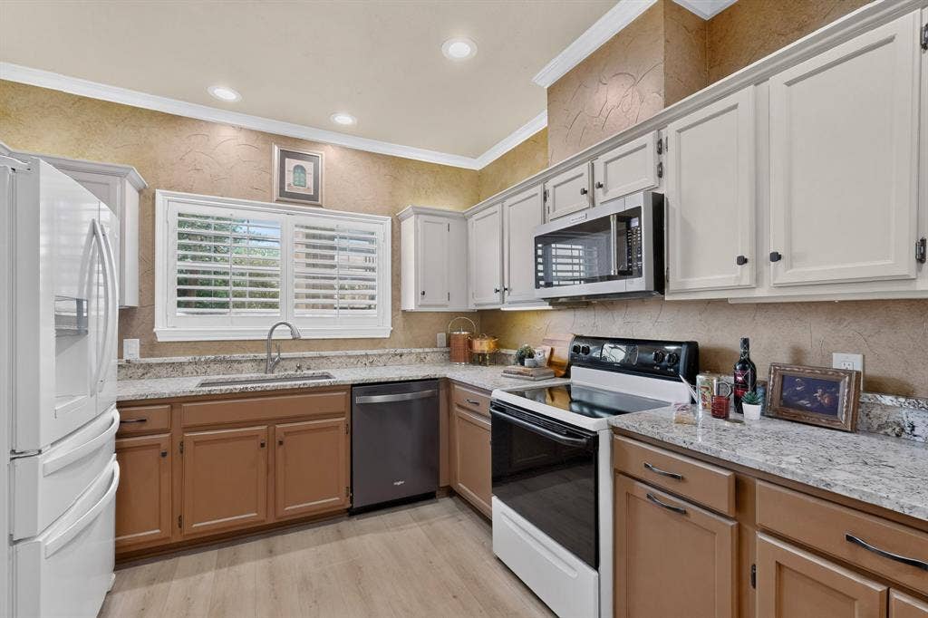 Kitchen featuring updated appliances, two-tone shaker-style cabinetry, light-toned stone countertops, built-in stainless steel microwave, recessed ceiling lighting, and plantation shutters.