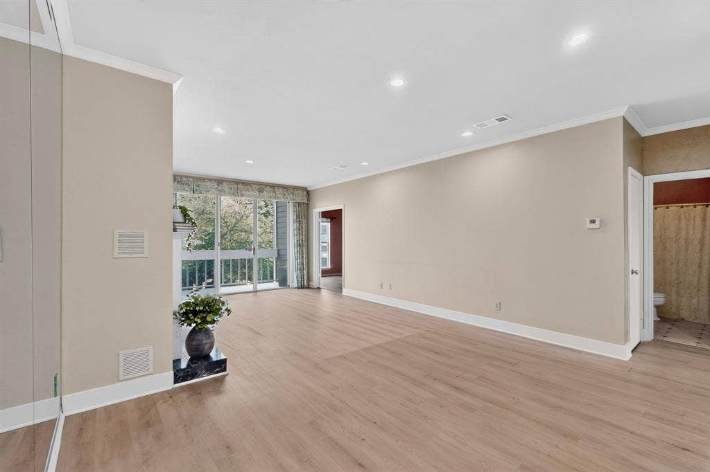 Open-concept interior featuring light wood-finish laminate flooring, recessed lighting, crown molding, a sliding glass door with a balcony, and a fireplace with a raised hearth.