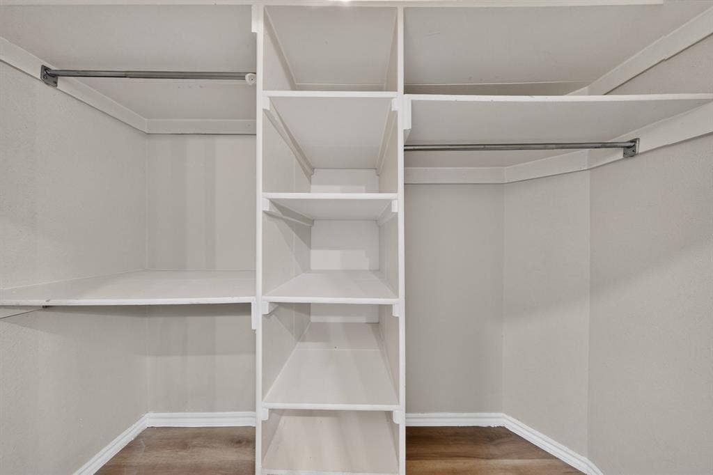Wrapped within the primary ensuite bathroom is this walk-in closet featuring built-in shelving, dual clothing rods, and newly installed wood-finish laminate flooring.