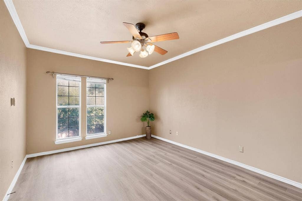 Primary bedroom featuring newly installed wood-finish laminate flooring, crown molding, and a ceiling fan with integrated light fixture.