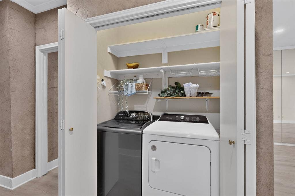 Laundry closet featuring dual folding doors and tiered shelving. Washer and Dryer are included in the sale.